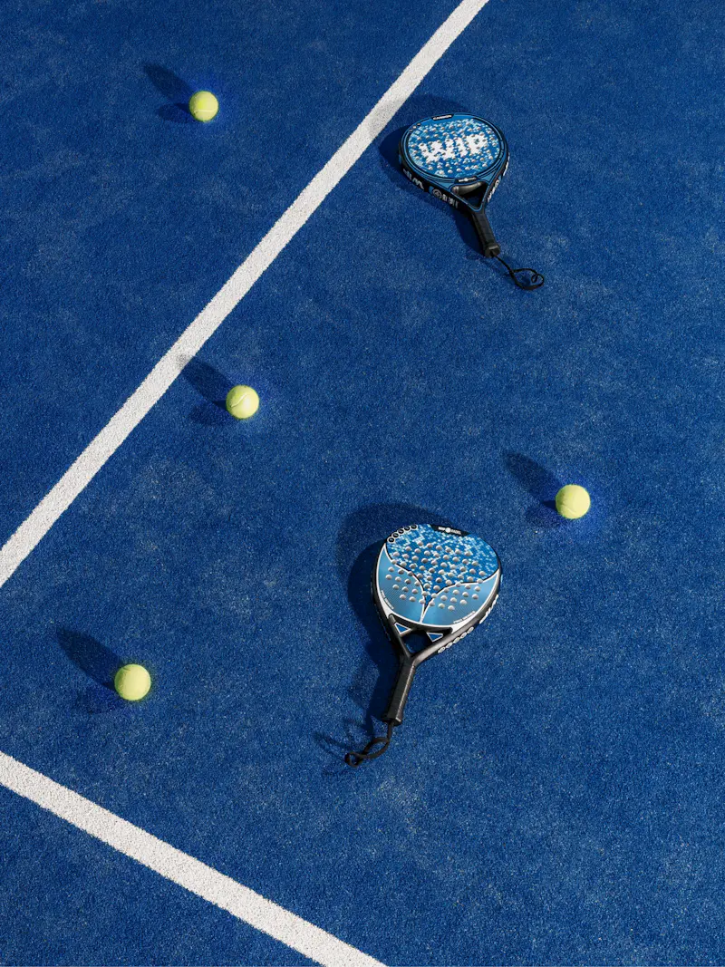 Dos palas de pádel y tres bolas sobre el césped azul de una cancha